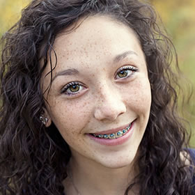 Young woman with braces smiling at camera, outdoor portrait with natural lighting