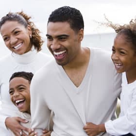 Happy family of four smiling together outdoors in white clothing near water.