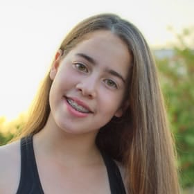 Young woman smiling outdoors with natural green background, professional headshot style portrait.