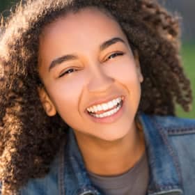Young woman smiling at camera wearing denim jacket in professional portrait setting.