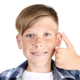 Young boy with braces smiling while talking on phone against white background