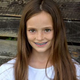 Young girl with braces smiling at camera against wooden background for orthodontics practice.