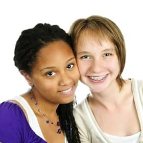 Two smiling teenage girls posing together against white background for orthodontics practice portrait.