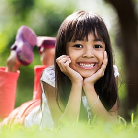 Young girl smiling at camera outdoors with toys in background, bright natural setting.