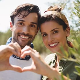 Smiling couple making heart shape with hands outdoors in sunny park setting.